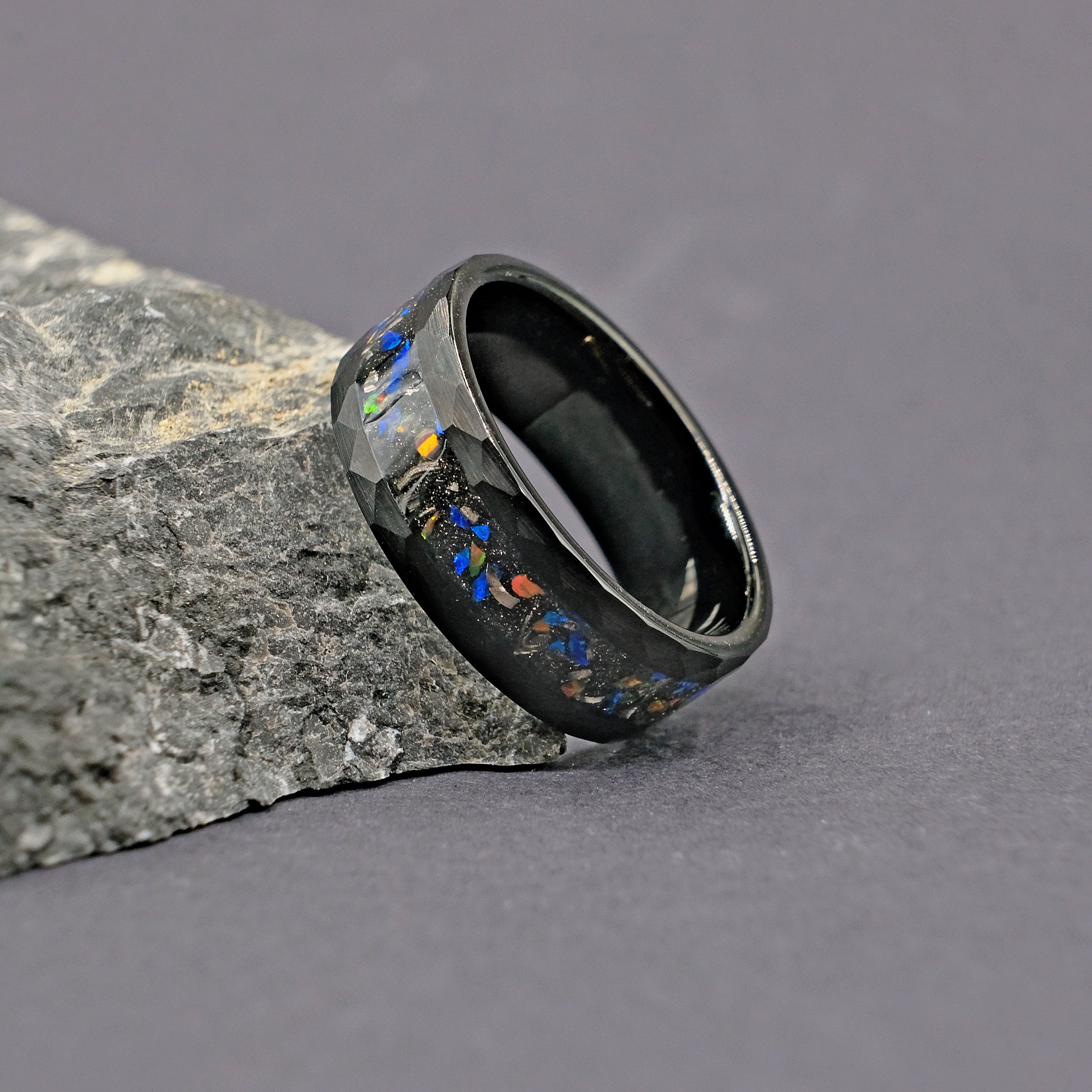 Meteorite Black Tungsten Opal Ring placed next to a rock, showcasing the intricate meteorite inlay and striking opal strip in a hammered tungsten band.
