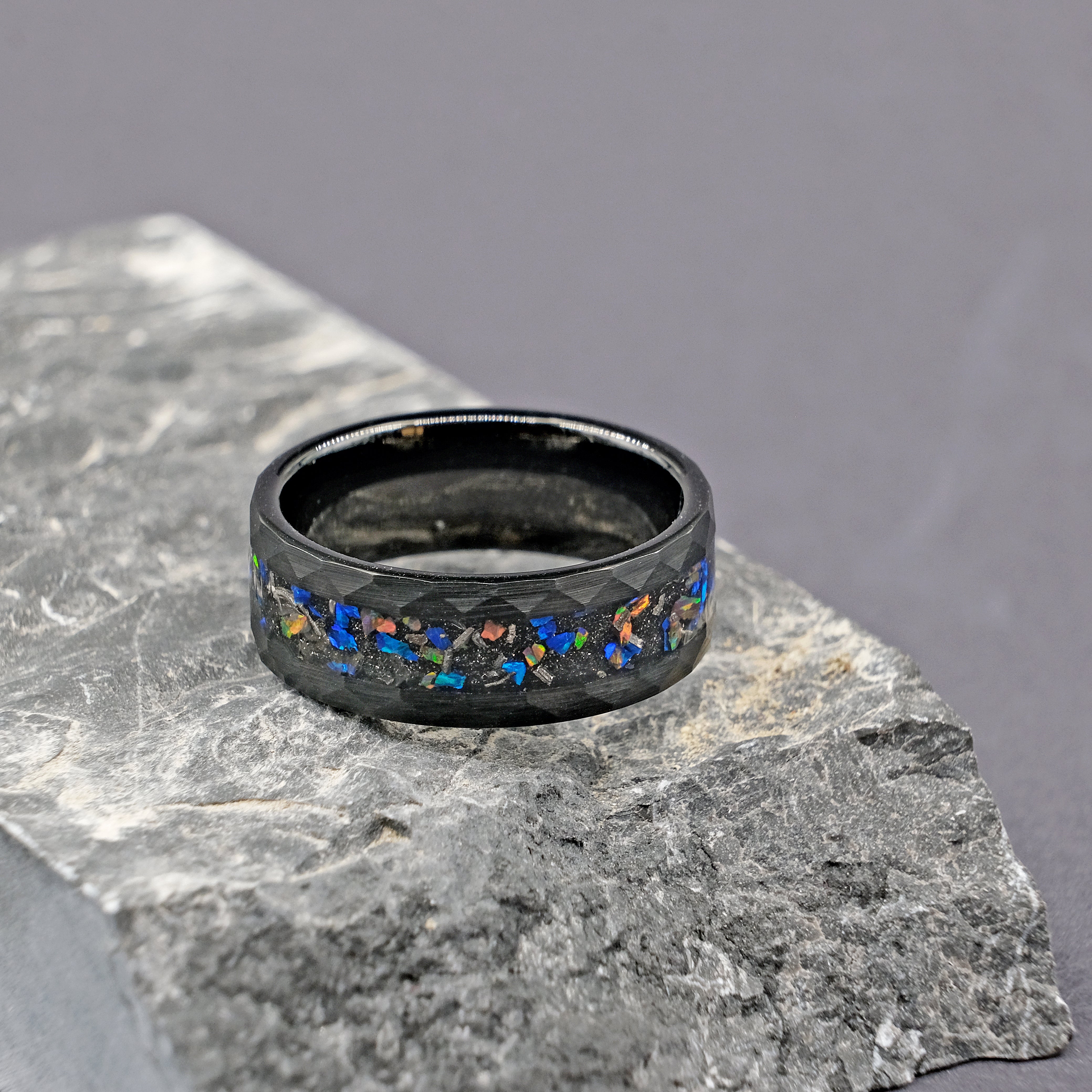 Side view of the Meteorite Black Tungsten Opal Ring next to a rock, highlighting the meteorite's distinct patterns and the polished opal strip.