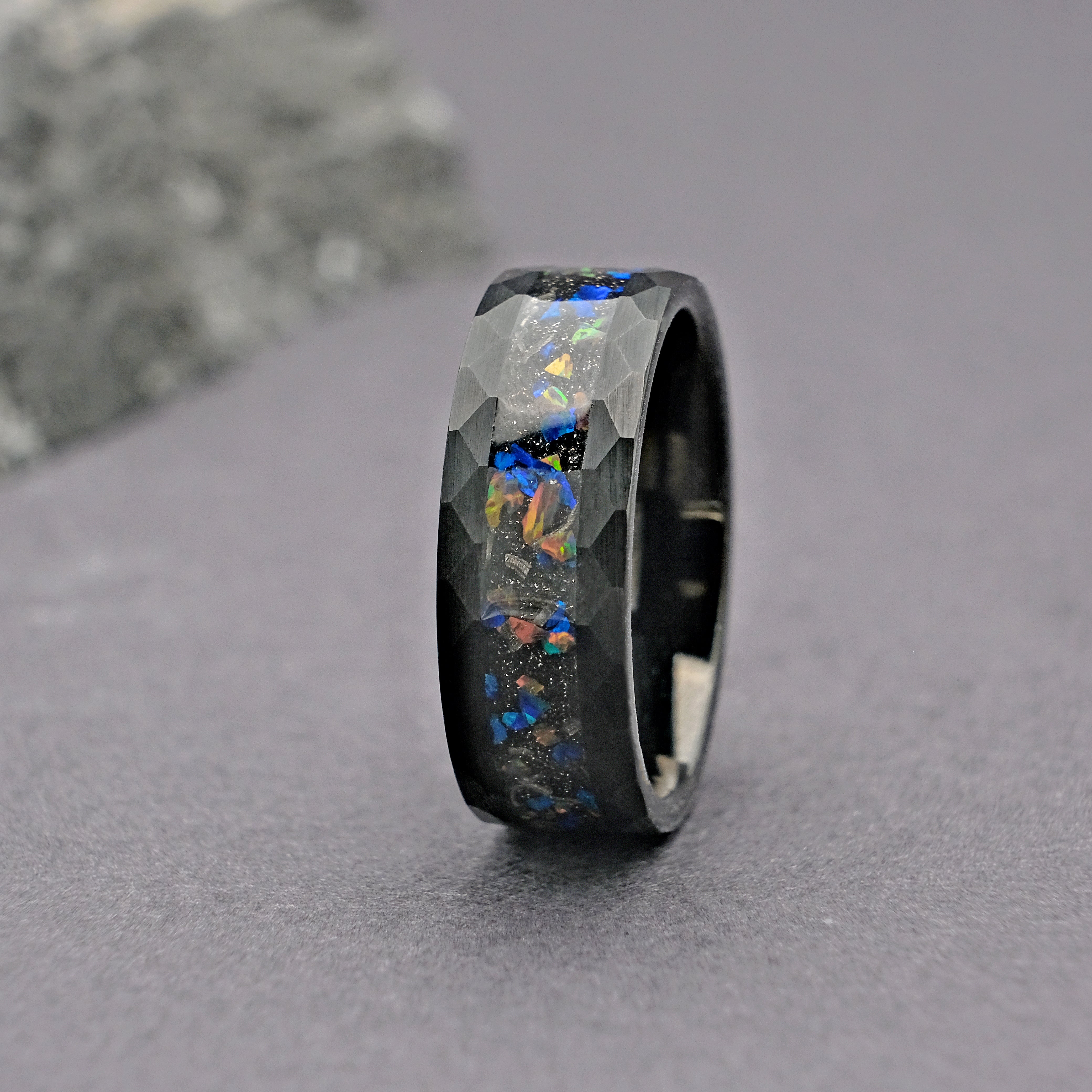 The Meteorite Black Tungsten Opal Ring, featuring a striking fusion of ancient meteorite inlay and a vibrant opal strip, masterfully set in a durable hammered tungsten carbide band.