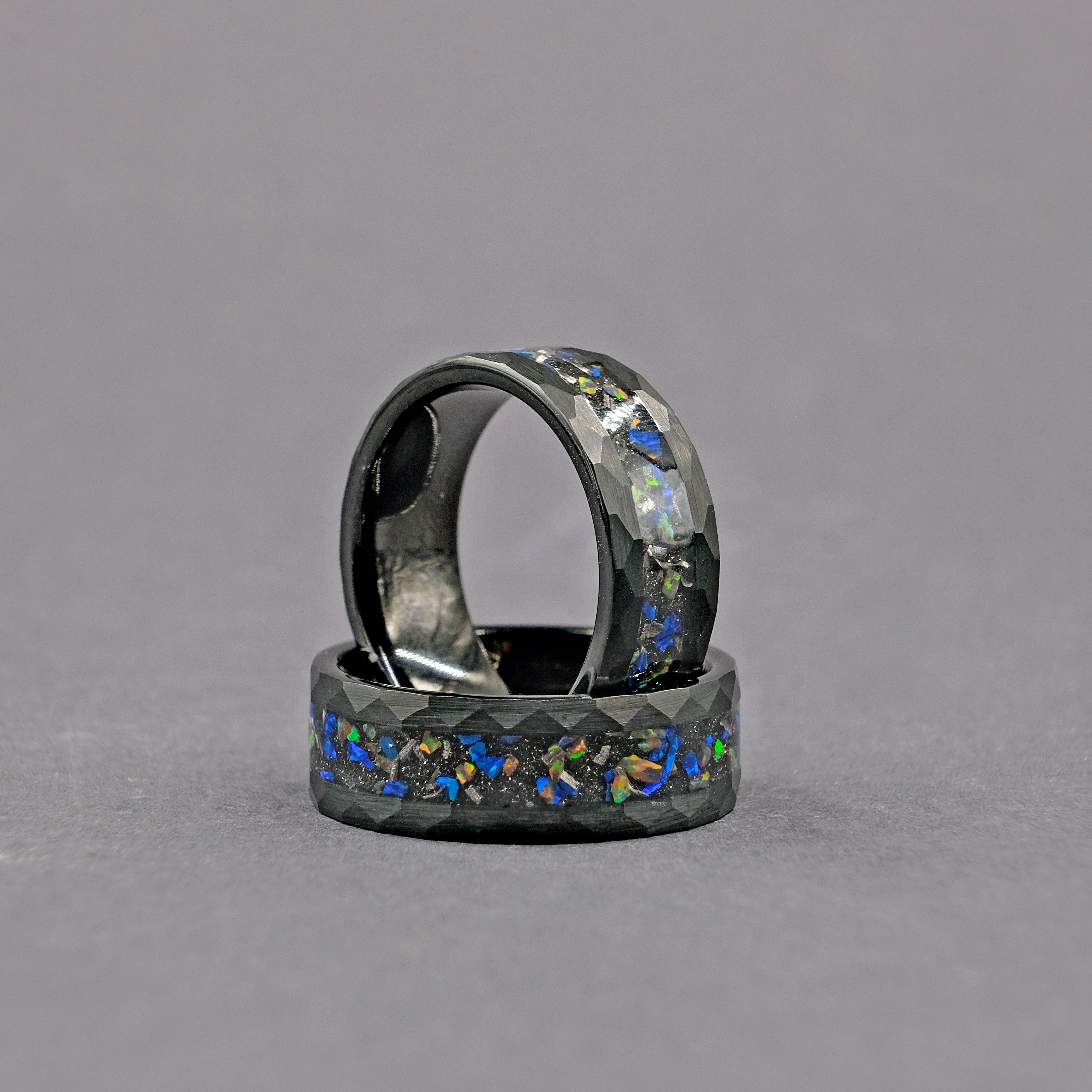 Close-up vertical shot of the Meteorite Black Tungsten Opal Ring, focusing on the detailed meteorite inlay and the luminous opal strip set within the hammered tungsten band.