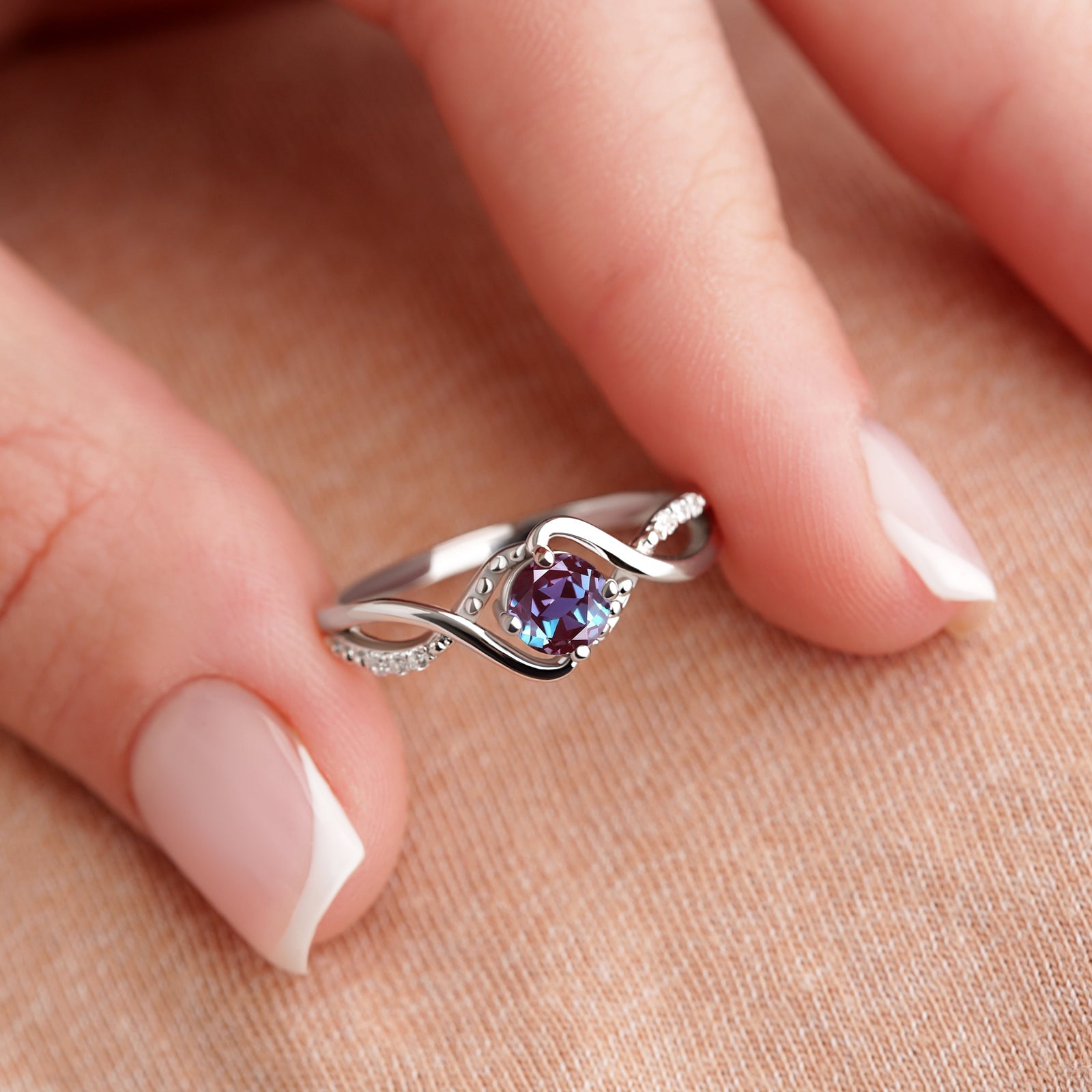 Silver Alexandrite Engagement Ring shown on a model's fingertips, emphasizing the unique gemstone and intricate craftsmanship.