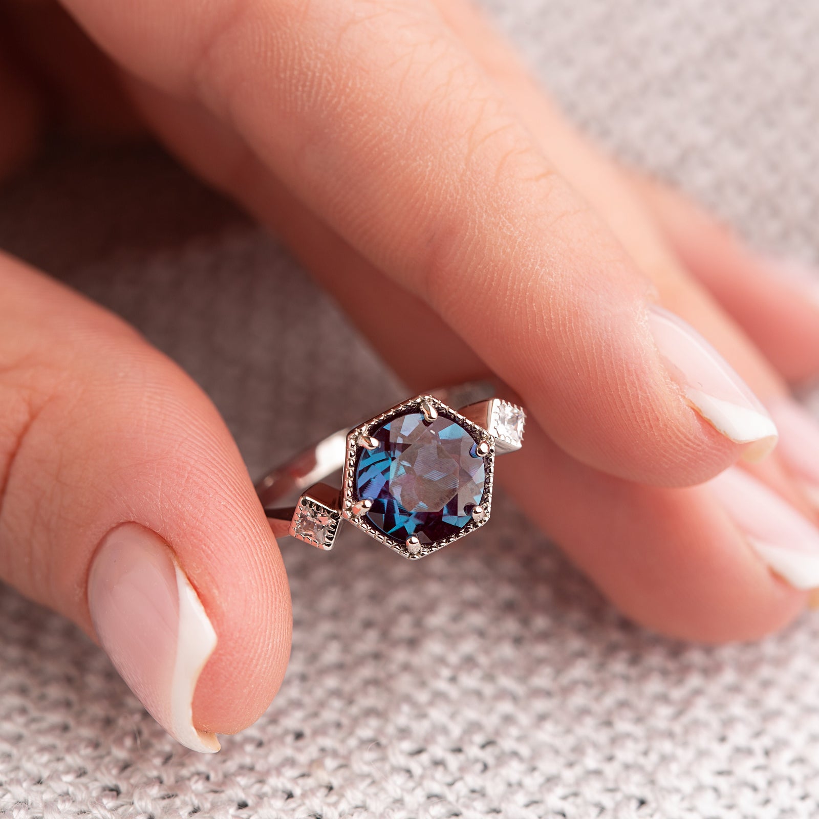 Close-up of the Swan Alexandrite Love Story Ring held at the fingertips, emphasizing the oval-cut Alexandrite and White Zircon accents.