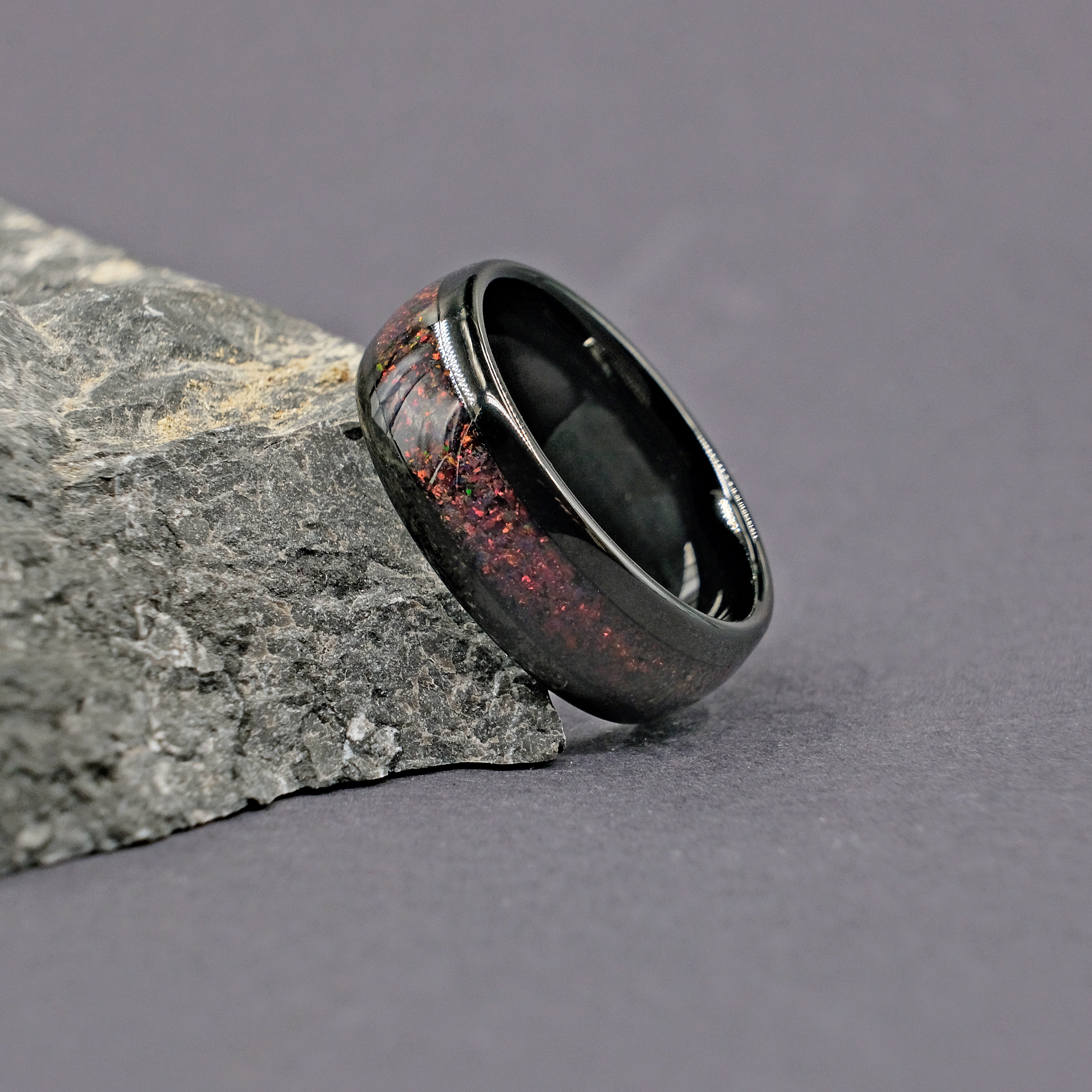 Black Tungsten Wedding Ring with Black Fire Opal inlay, elegantly placed next to a natural rock for a stylish contrast.