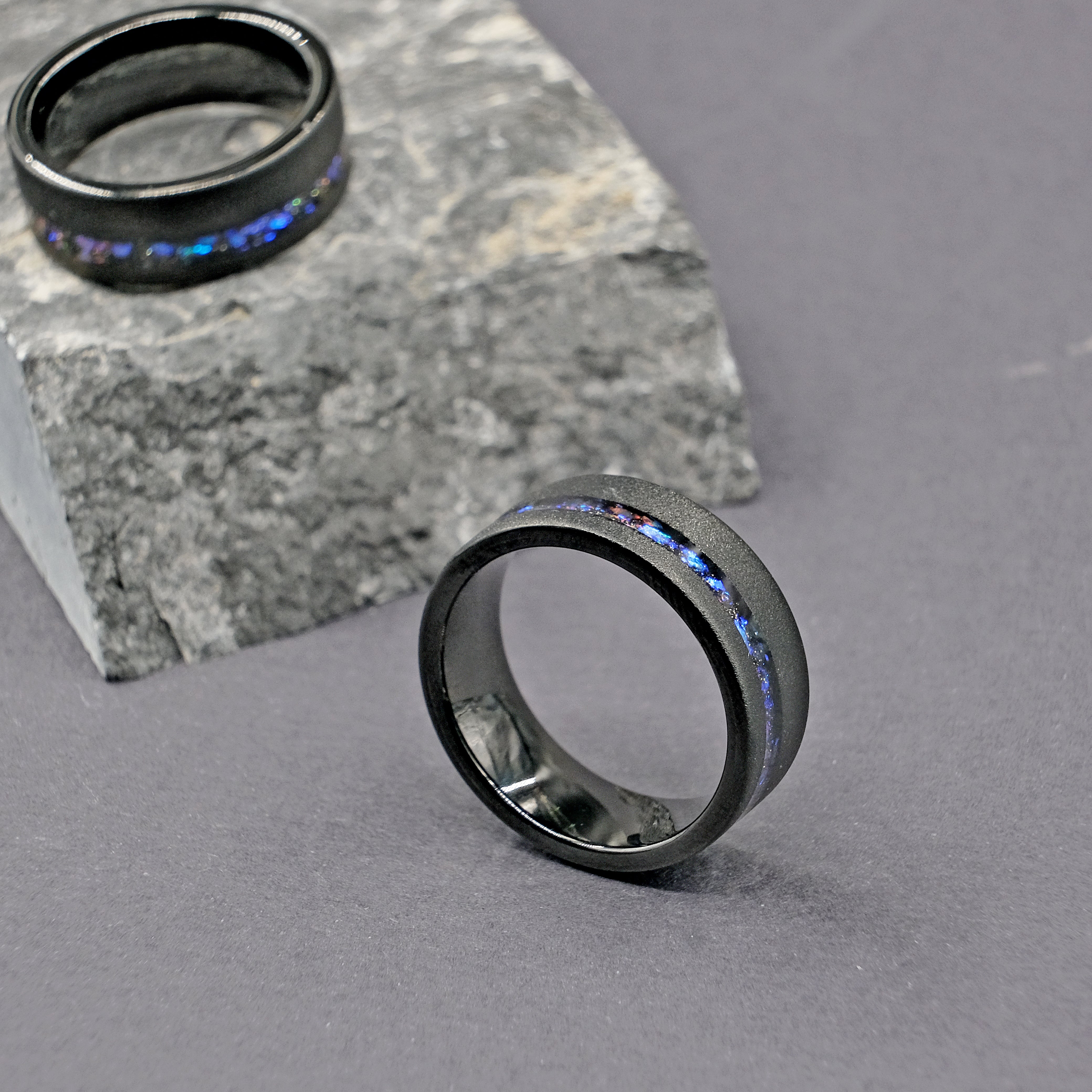 Set of Domed Galaxy Opal Wedding Rings placed on top of a rock, displaying their cosmic opal inlays and sturdy tungsten carbide bands.