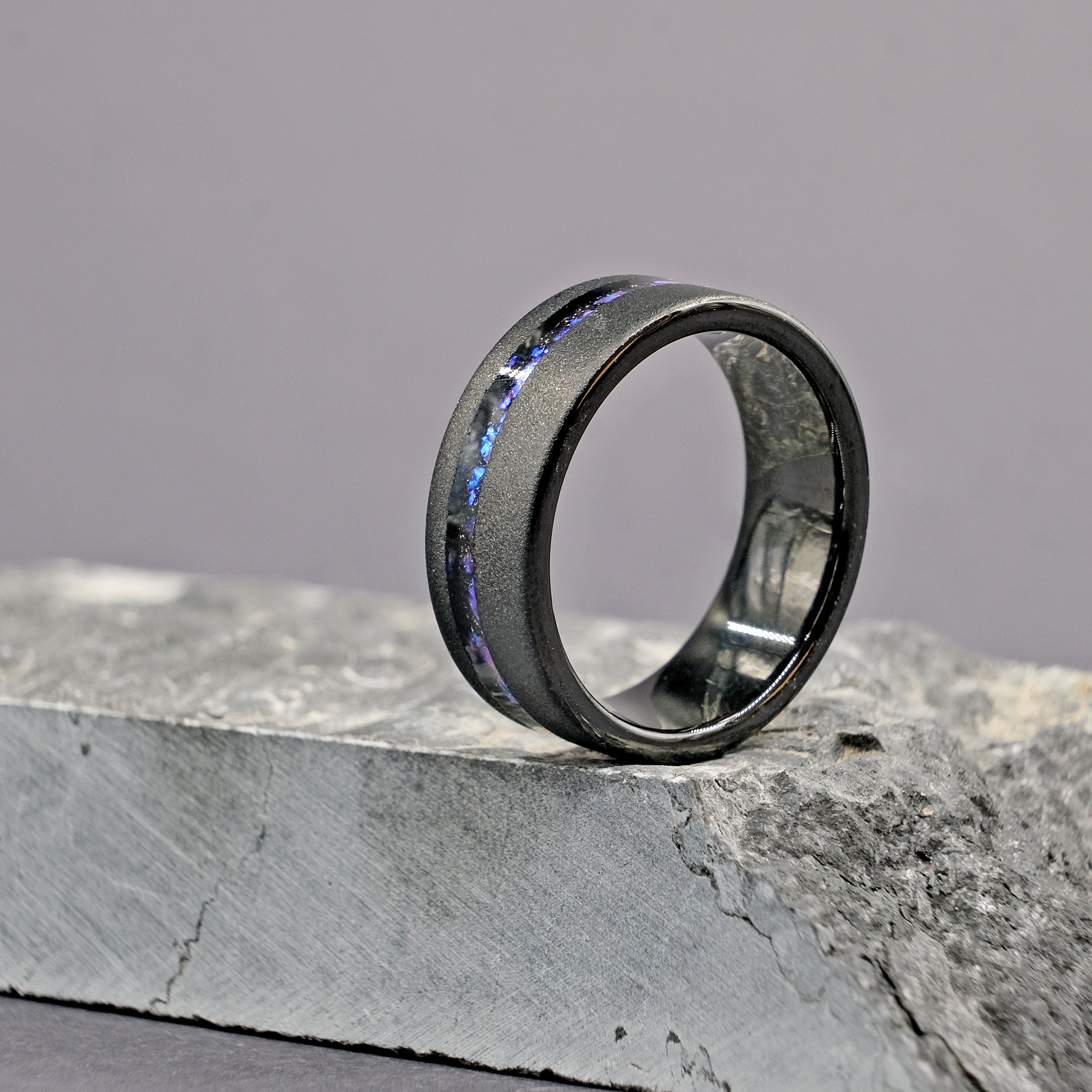 Domed Galaxy Opal Wedding Ring placed next to a rock, showcasing its opal inlay and robust tungsten carbide band.