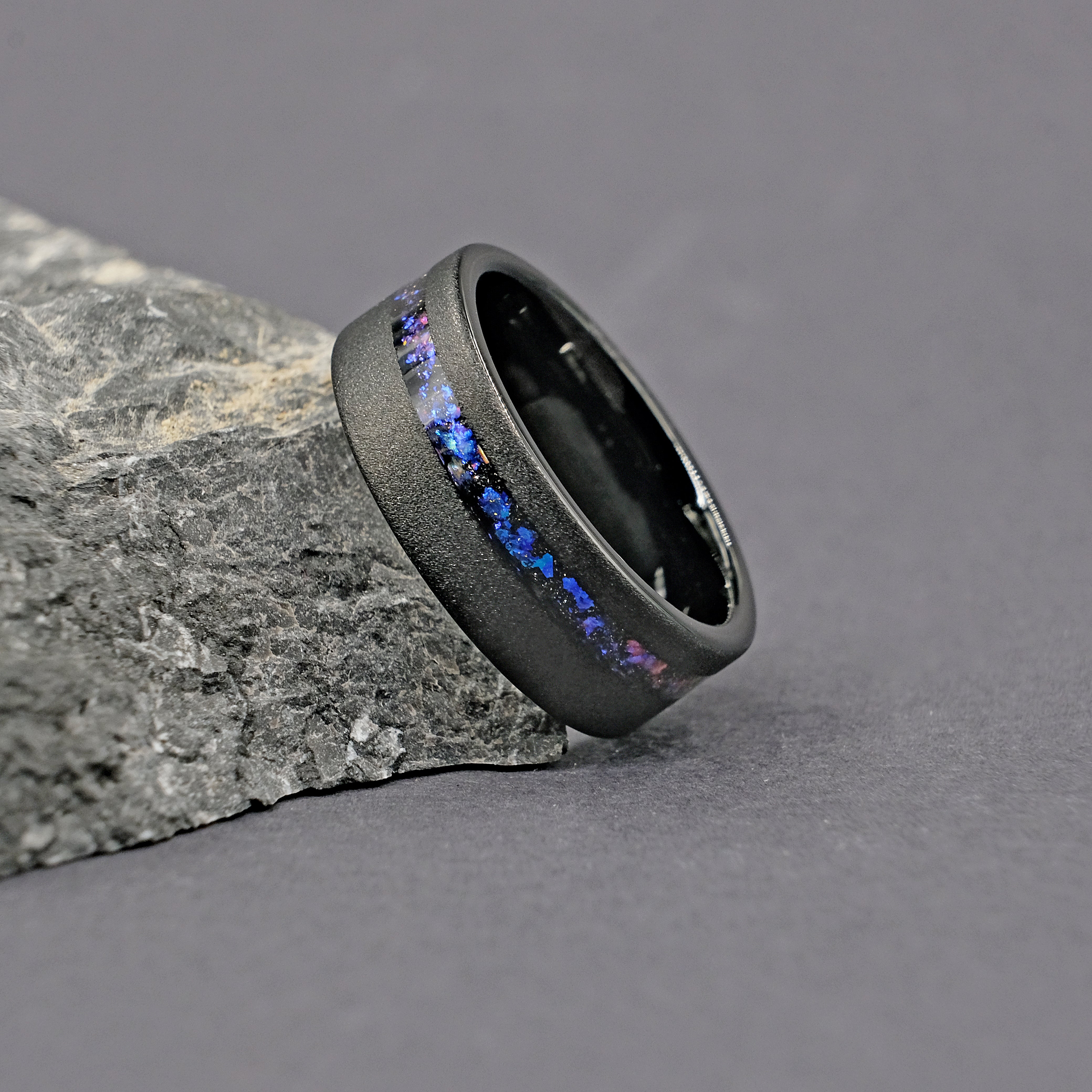 Side view of the Domed Galaxy Opal Wedding Ring next to a rock, highlighting the galaxy opal inlay and durable tungsten carbide.