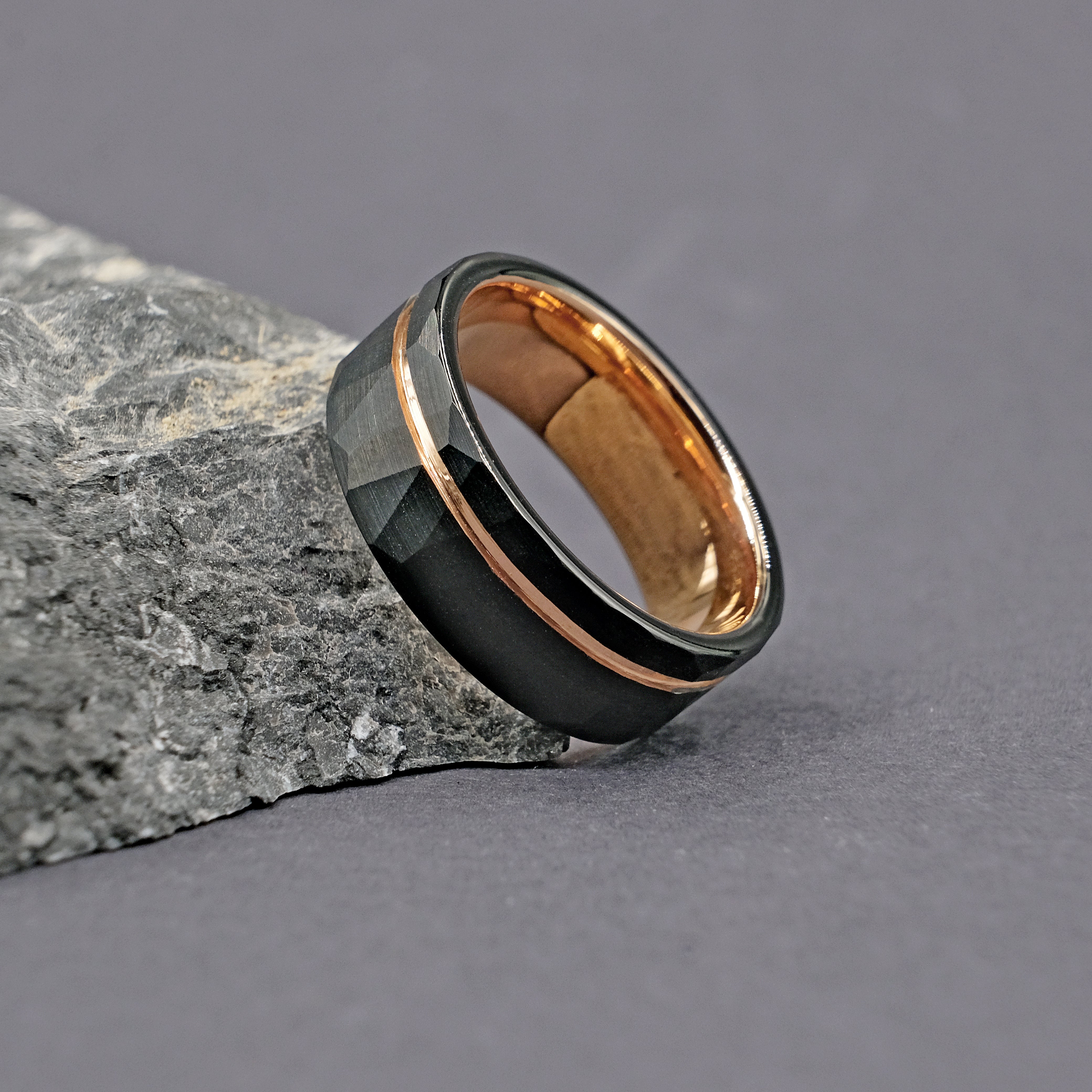 Hammered Black Strip Men Ring placed next to a rock, showcasing its rugged hammered finish and sleek gold strip.