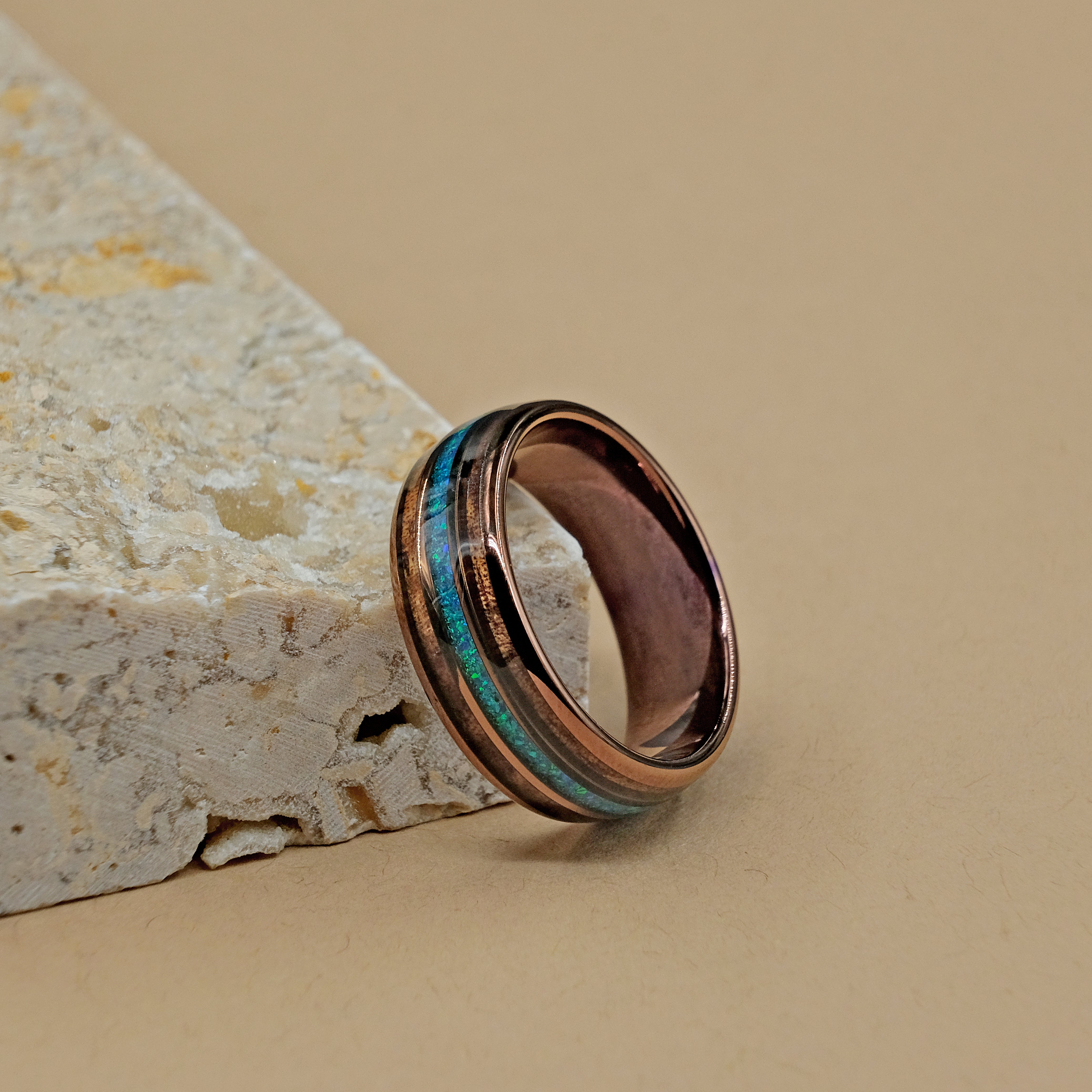 Side view of the Hawaiian Koa Wood Wedding Ring next to a rock, emphasizing the craftsmanship of the opal and wood inlays within the durable tungsten carbide shell.