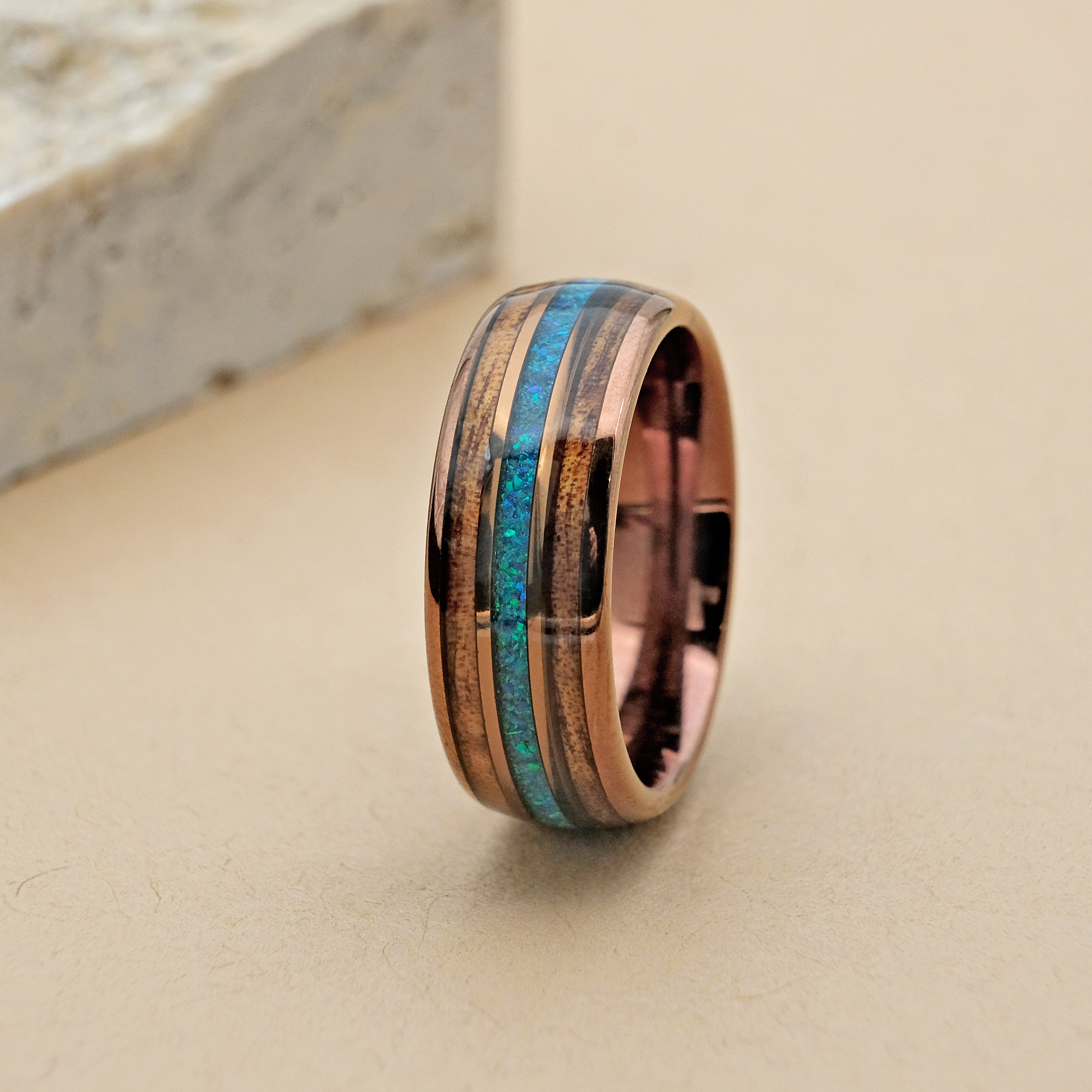 Close-up vertical shot of the Hawaiian Koa Wood Wedding Ring, highlighting the detailed craftsmanship of the Koa wood and opal inlays and the luxurious rose gold finish.