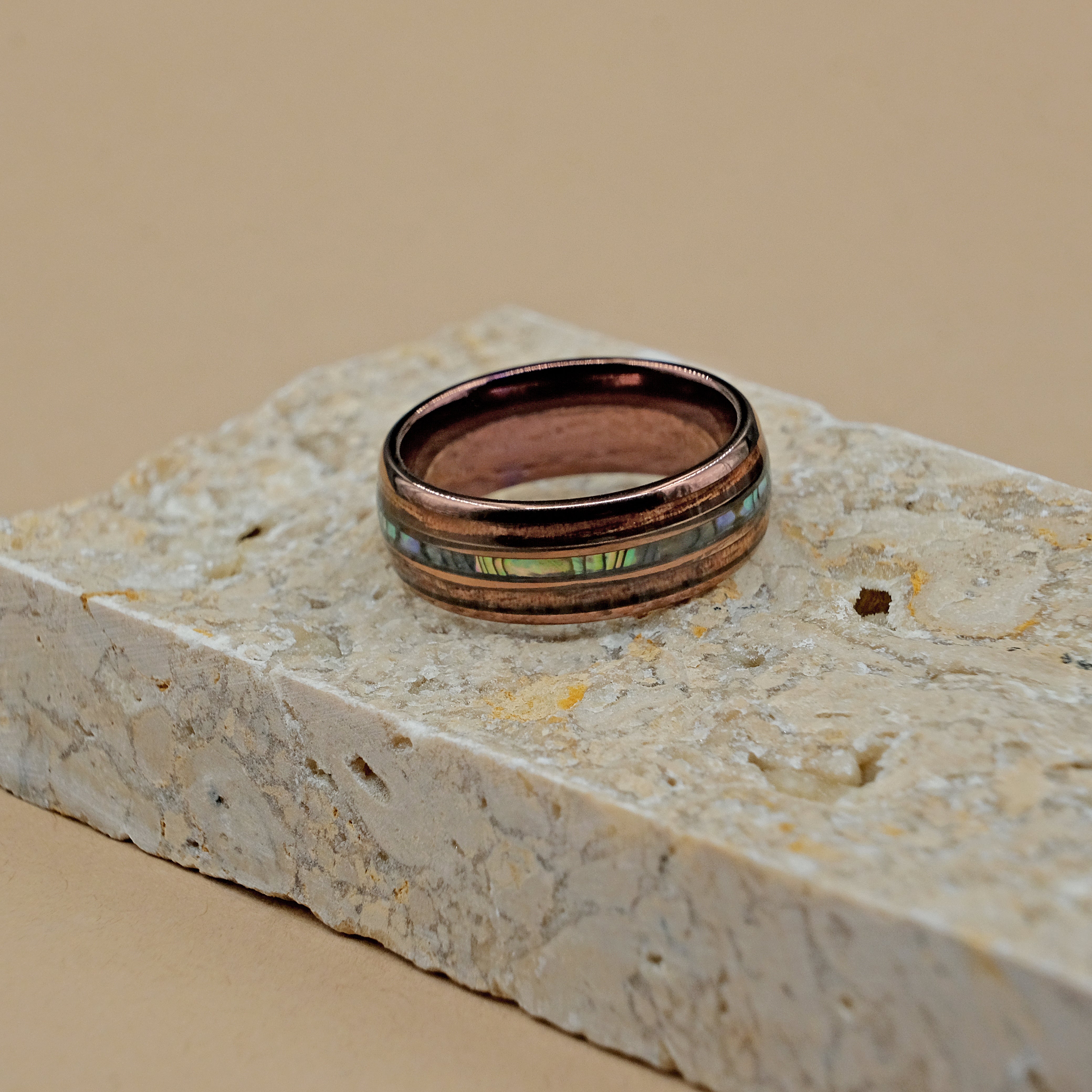 Hawaiian Tungsten Ring placed next to a rock, showcasing the exquisite craftsmanship of the Koa wood and Bello Opal inlays within the durable tungsten carbide shell.