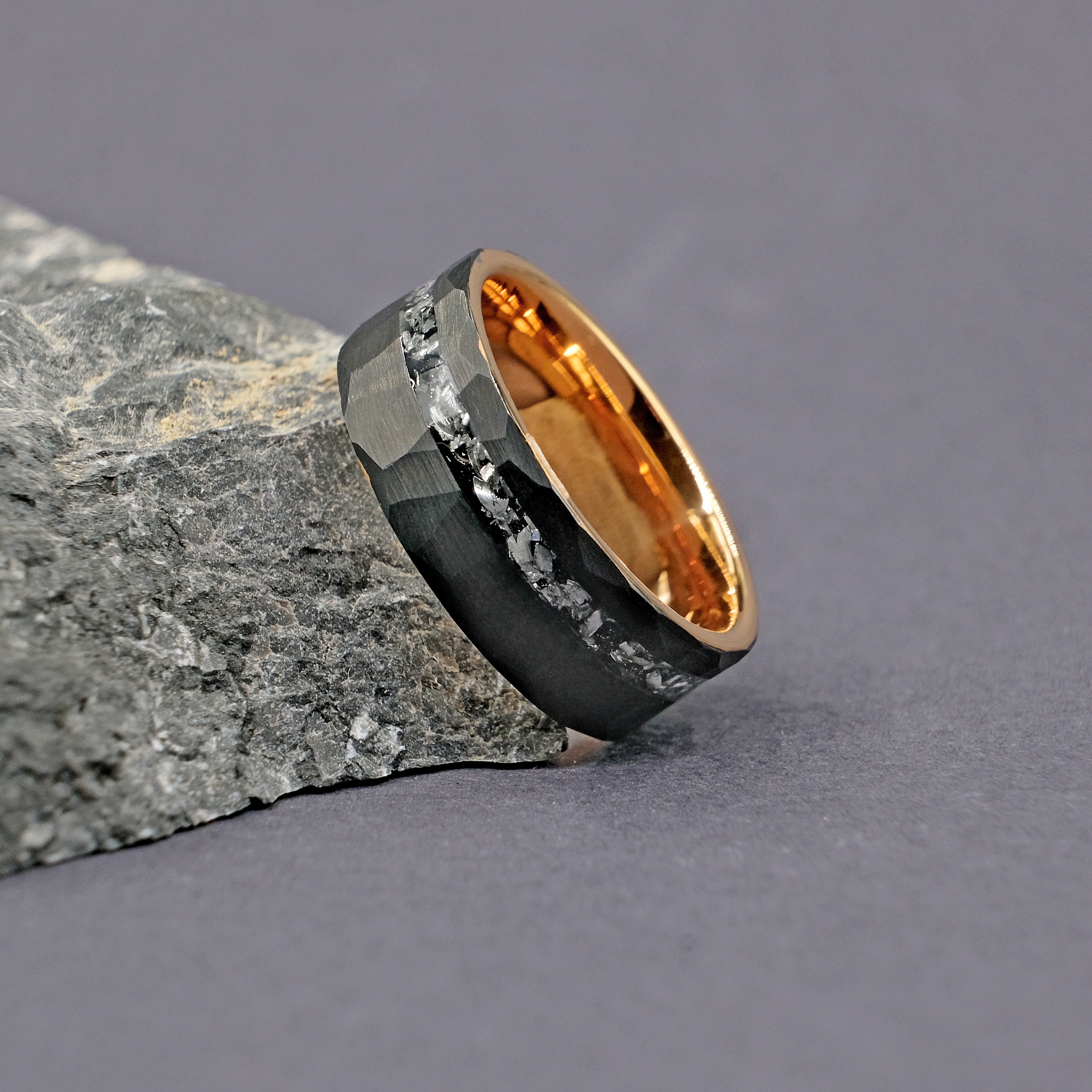 Meteorite Black Artisan Tungsten Ring placed next to a rock, emphasizing the unique crystalline structure of the Muonionalusta meteorite inlay.