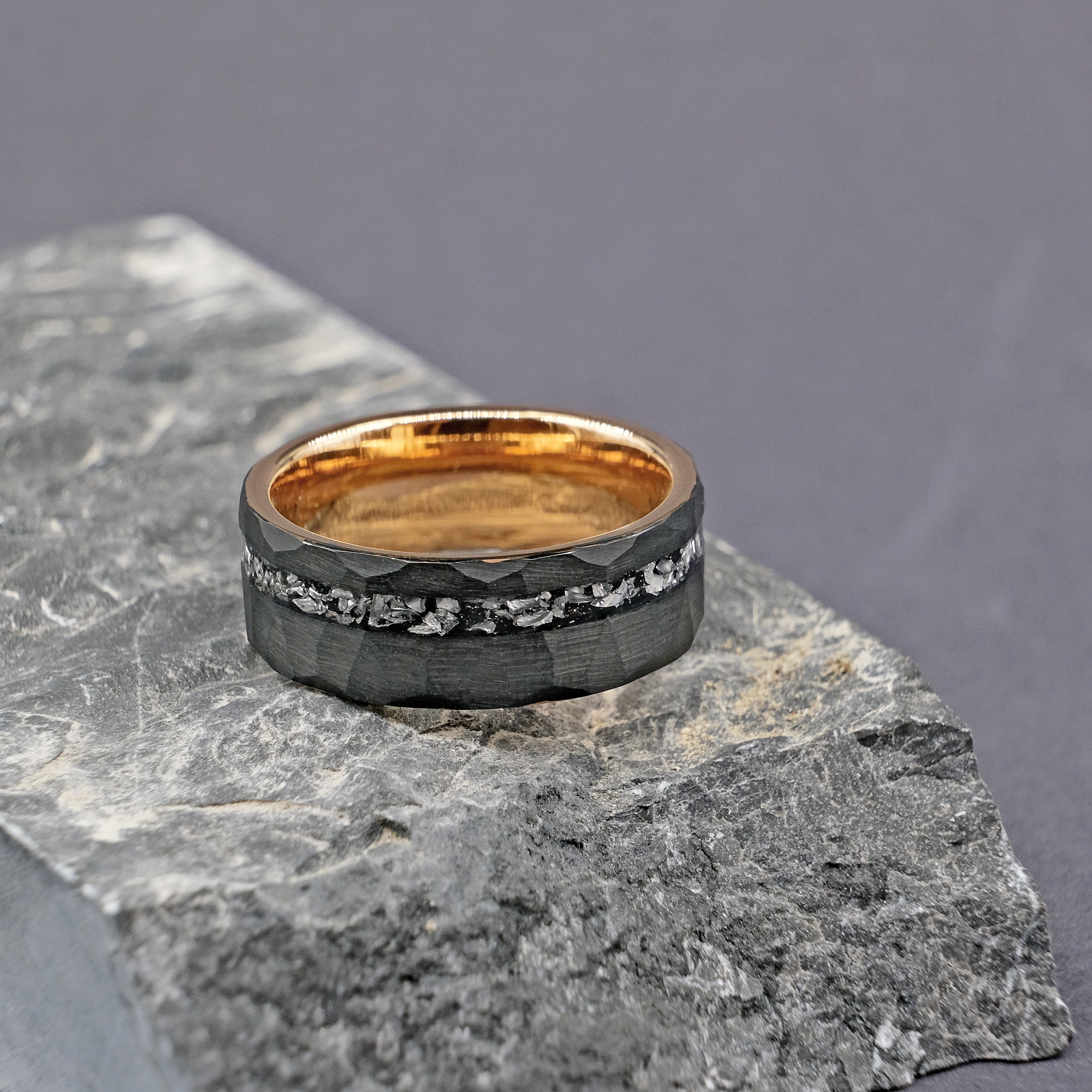 Side view of the Meteorite Black Artisan Tungsten Ring next to a rock, showcasing the intricate meteorite patterns and the modern tungsten carbide band.