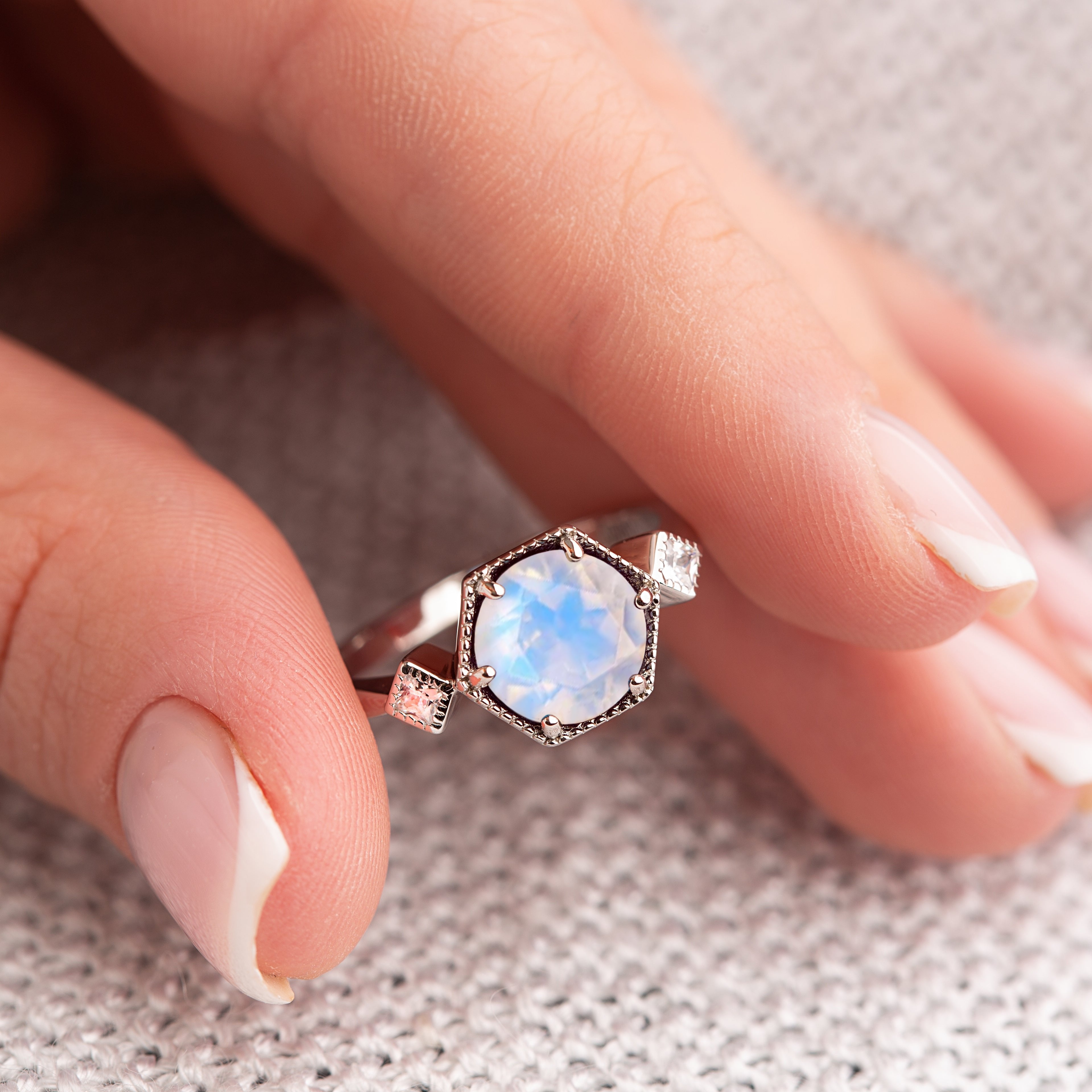 Close-up of intricate floral moonstone ring on fingertip, showcasing hexagon gemstone and sterling silver details