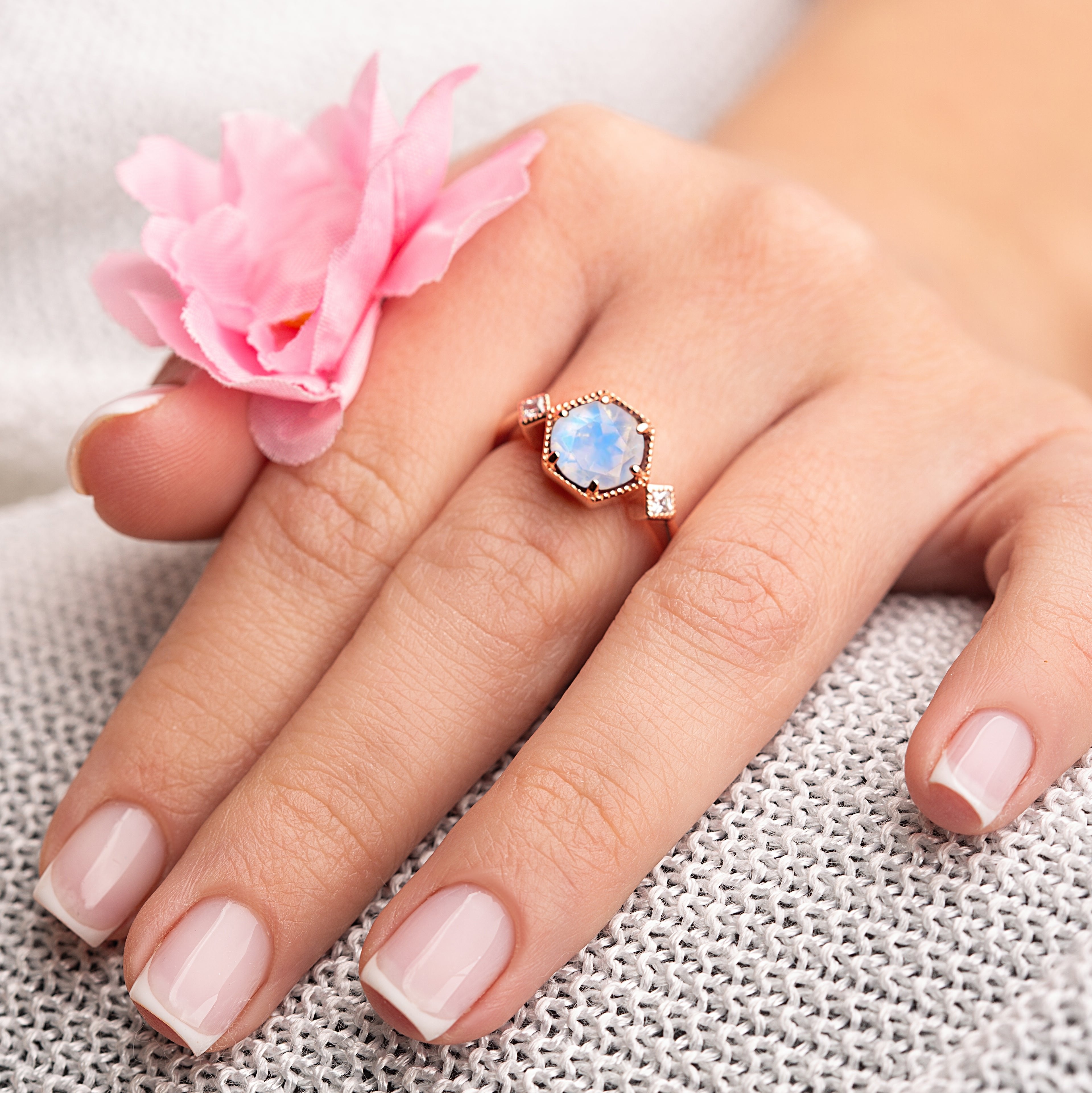 Model displaying hexagon-cut moonstone wedding ring, surrounded by pink floral accents, symbolizing elegance and love