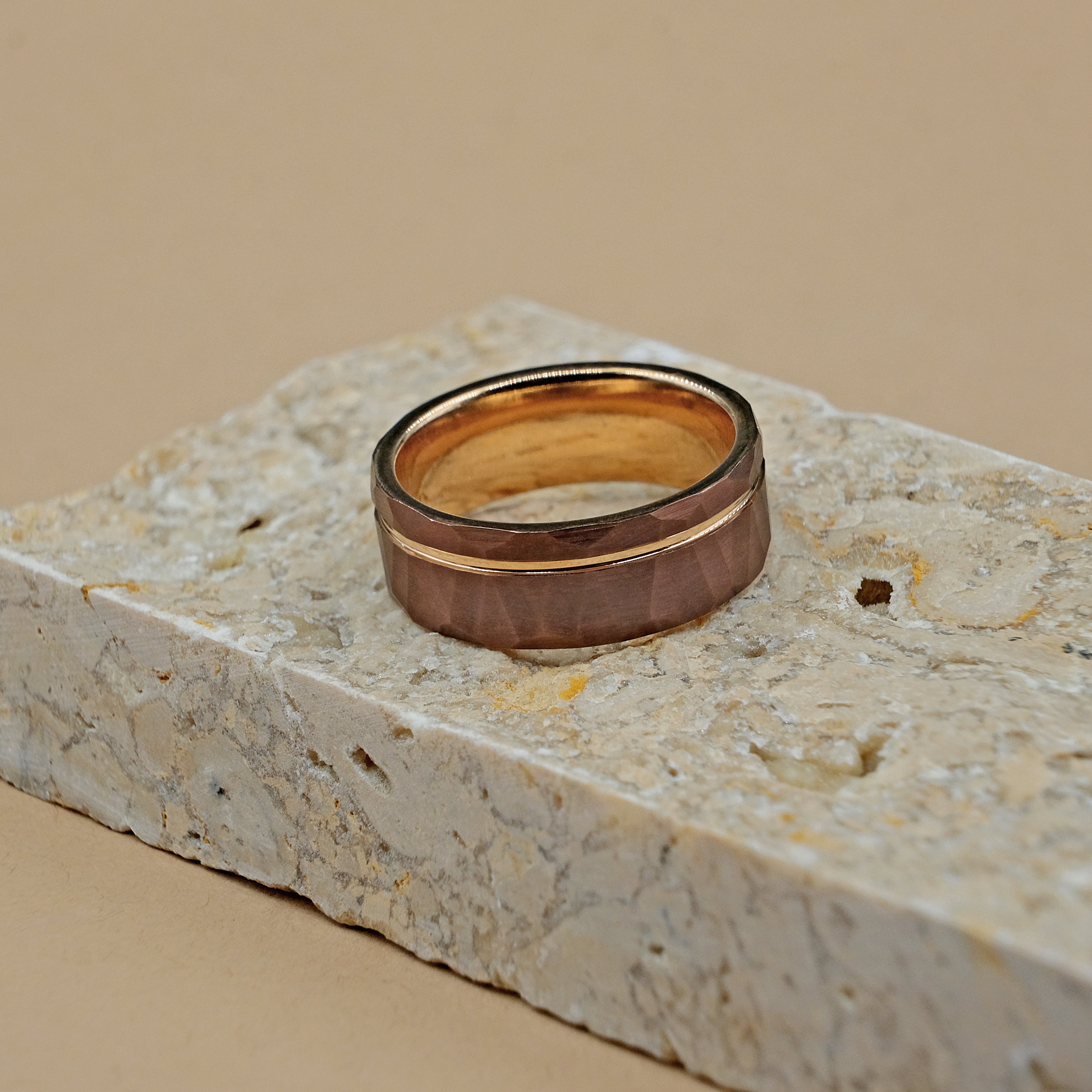 Rose Gold Hammered Tungsten Ring placed horizontally on  to a natural rock, emphasizing its rugged durability and refined appearance.