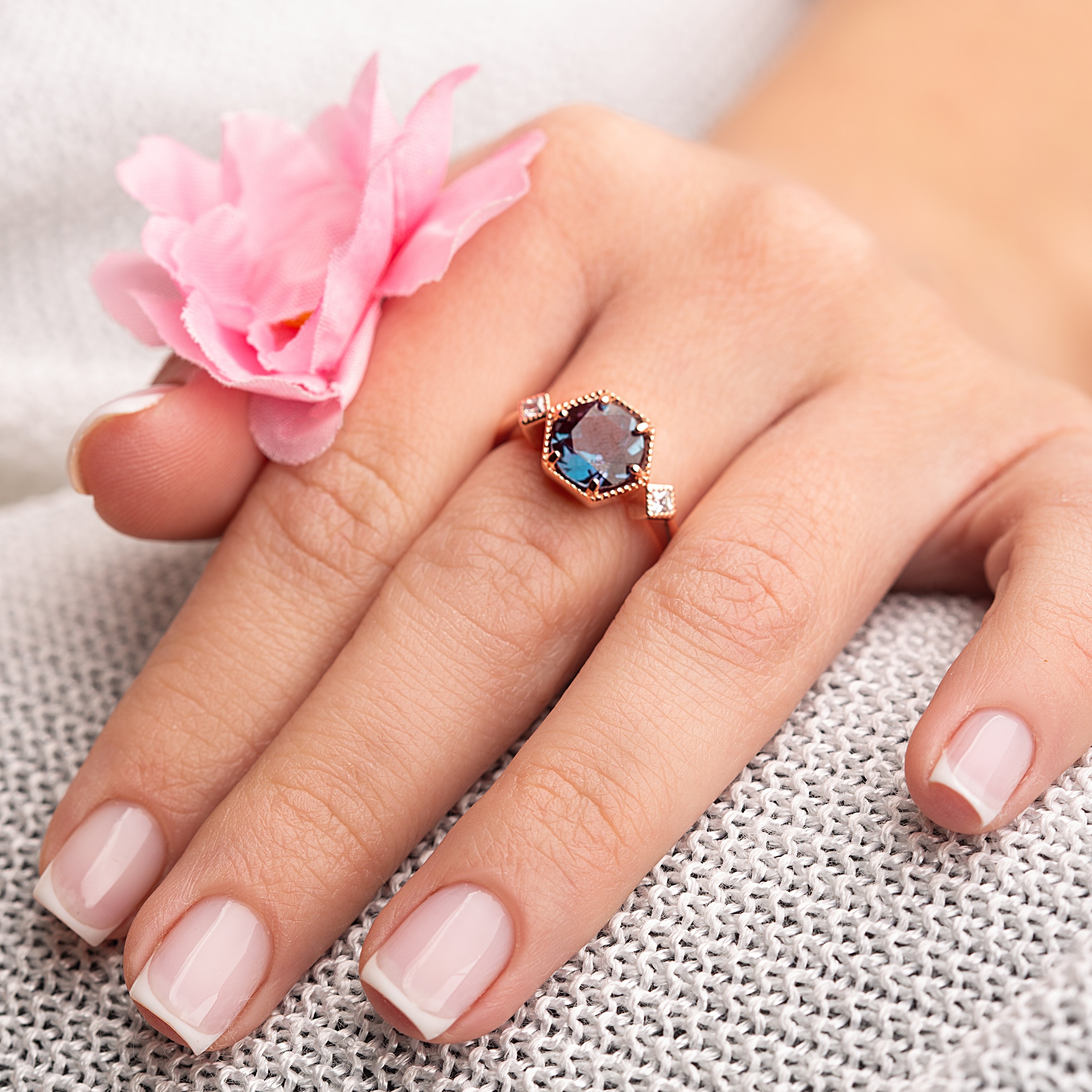 Model wearing the Swan Alexandrite Love Story Ring with flowers, showcasing the 8x8mm color-changing Alexandrite gemstone