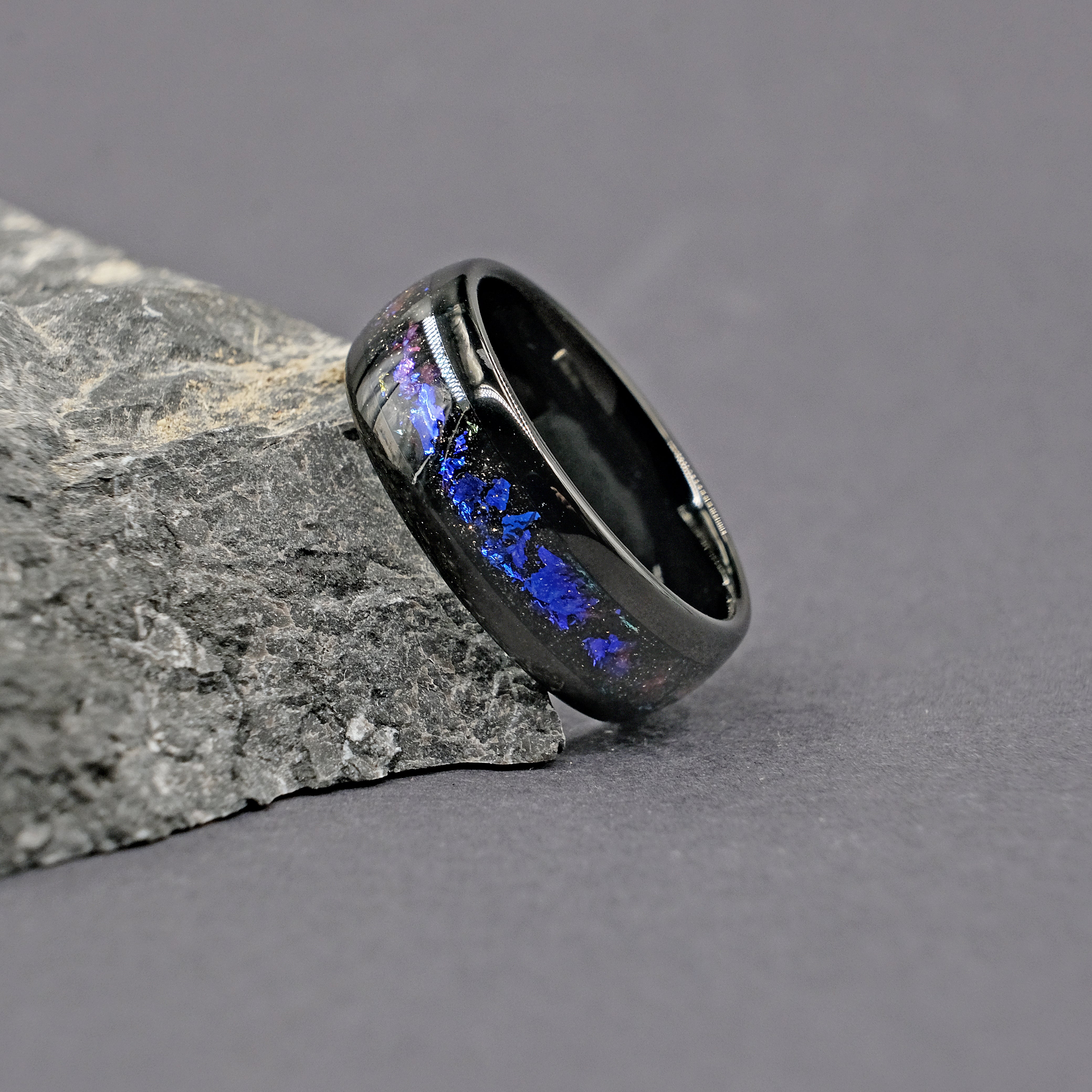 Single Unique Aqua Tungsten Wedding Ring placed next to a rock, showcasing the vibrant Galaxy Opal against a natural backdrop.