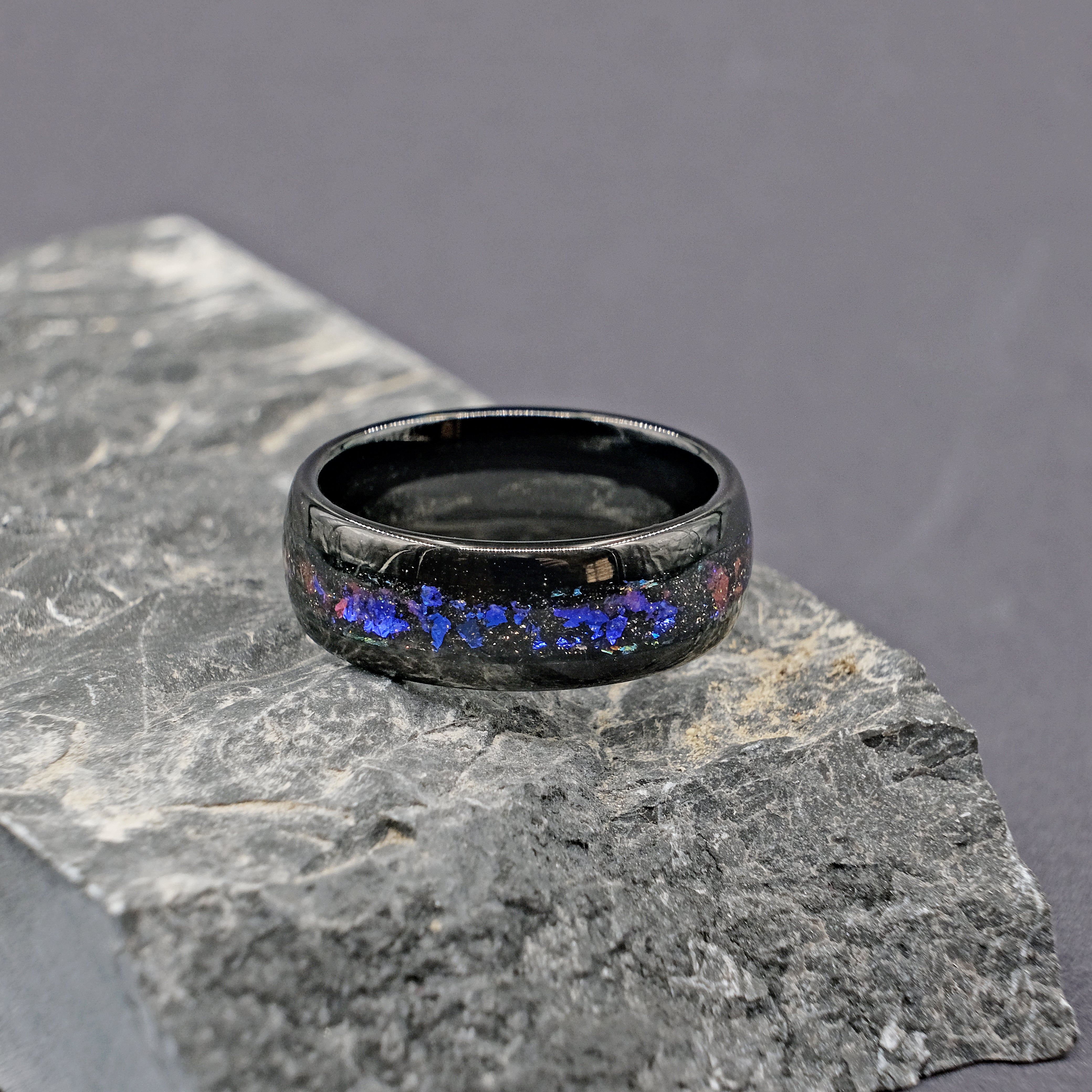 Unique Aqua Tungsten Wedding Ring placed on a rock, emphasizing the rugged durability and stunning opal centerpiece.