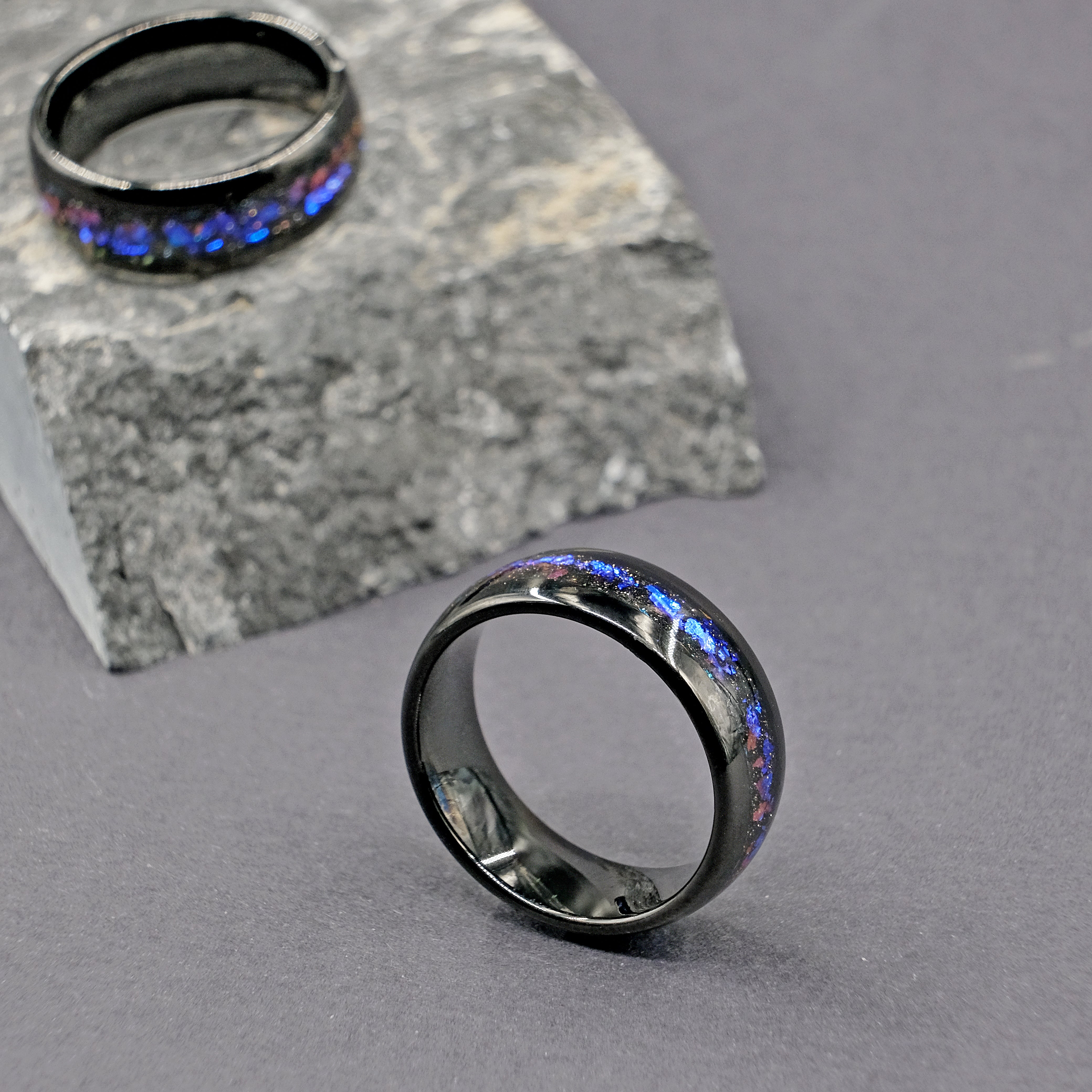 A set of Unique Aqua Tungsten Wedding Rings displayed on a rock, highlighting their bold design and Galaxy Opal beauty.