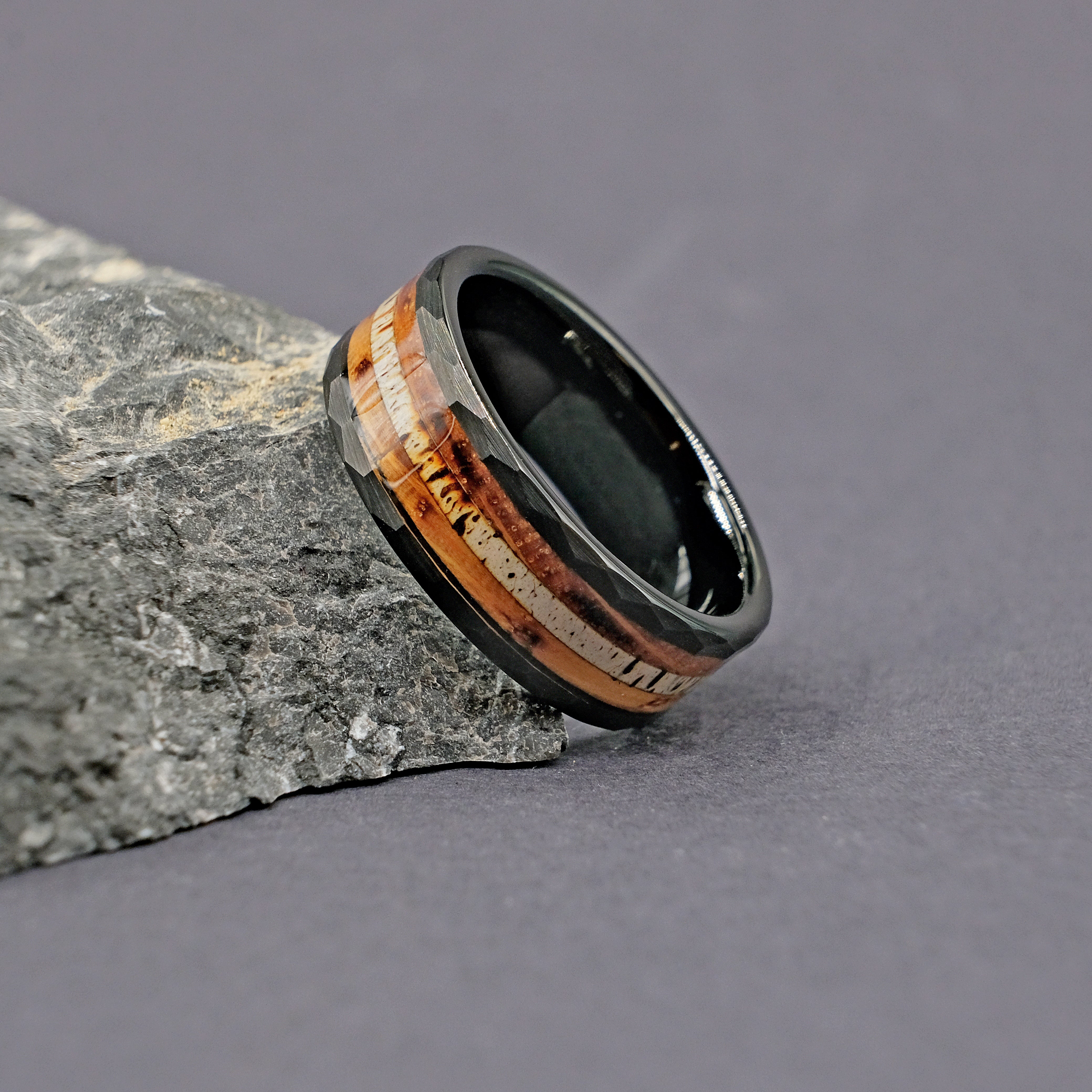 Whiskey Barrel Wedding Ring with wood inlay, placed next to a rock, emphasizing its natural and rugged design.