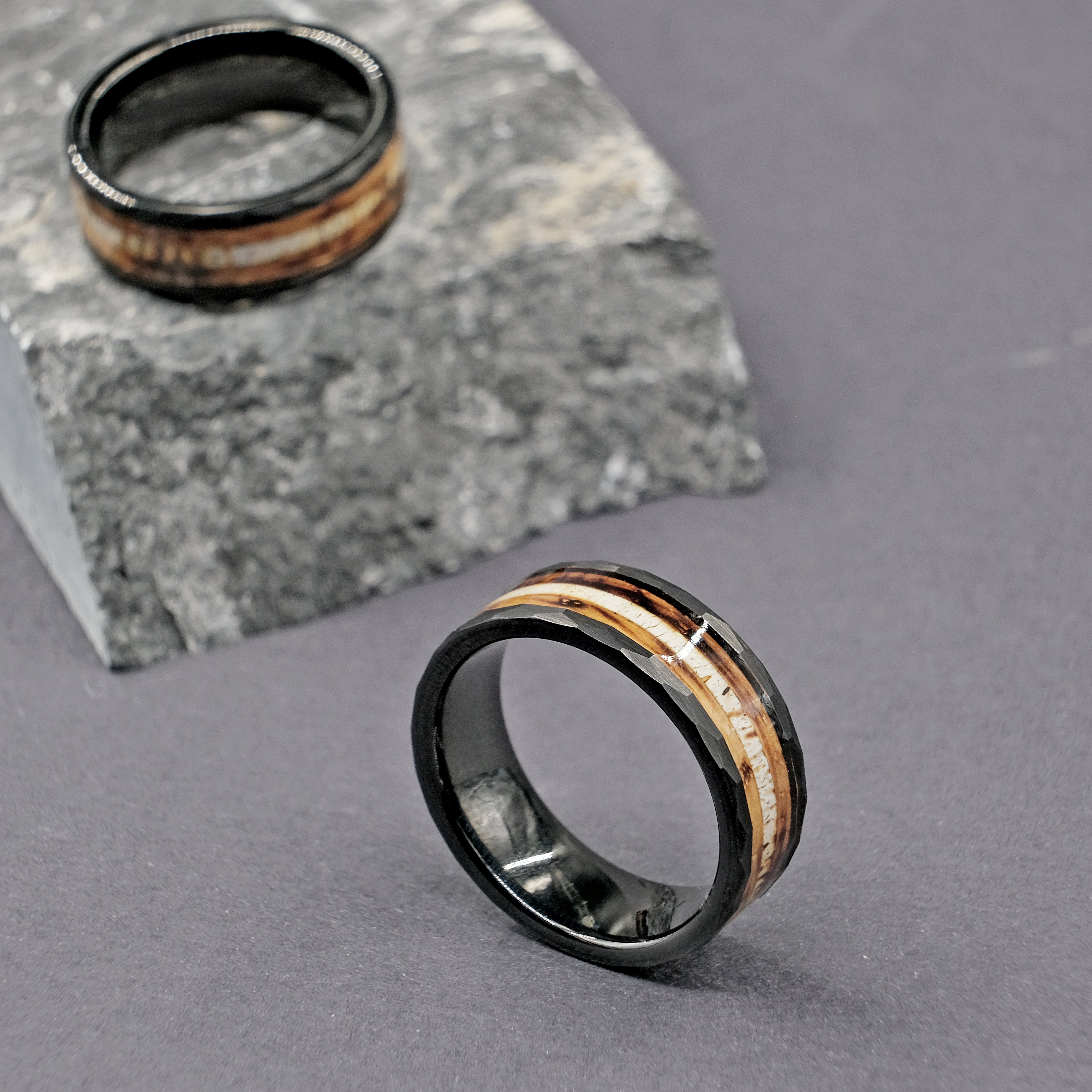 Set of Whiskey Barrel Wedding Rings, elegantly displayed next to a natural rock to highlight the rustic wood inlay.